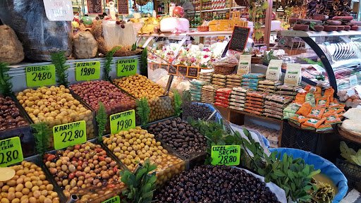 A colorful stall of fresh fruits and vegetables at Kadıköy Market, with vendors and passersby.