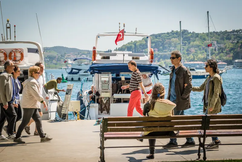 People strolling on the Bebek Sahili (seaside promenade) on a sunny day, with yachts in the background.
