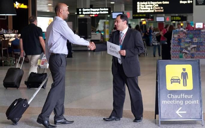 Driver welcoming passengers with a name sign at Istanbul Airport, comfortable vehicle in the background.