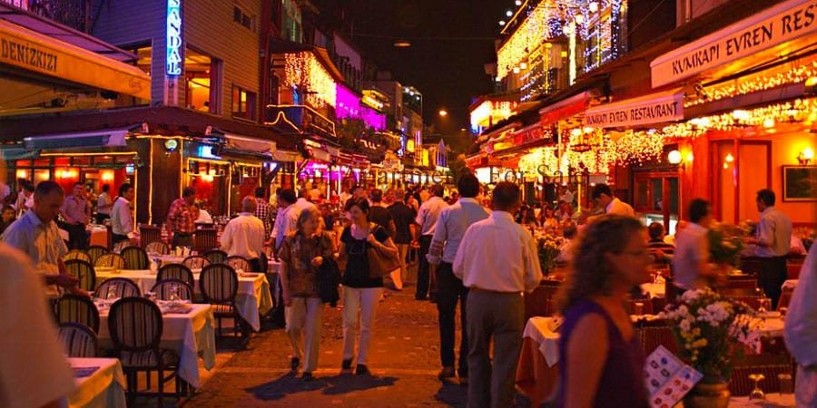 Rue animée de Taksim la nuit, avec des restaurants illuminés et des gens profitant de la vie nocturne.